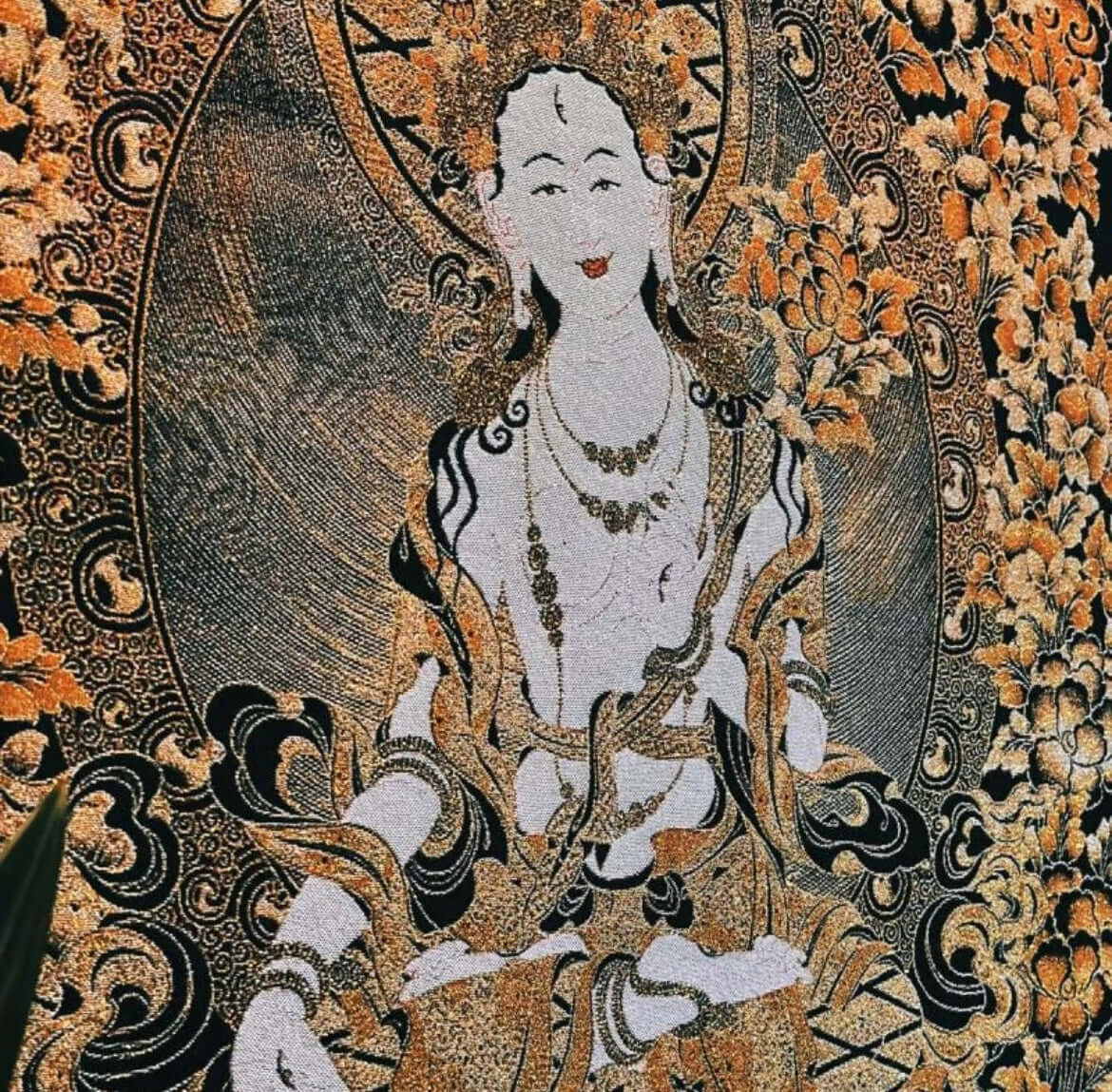 White Tara Thangka Wall Art displayed in a frame, radiating compassion and spiritual renewal against a bold red wall. 3