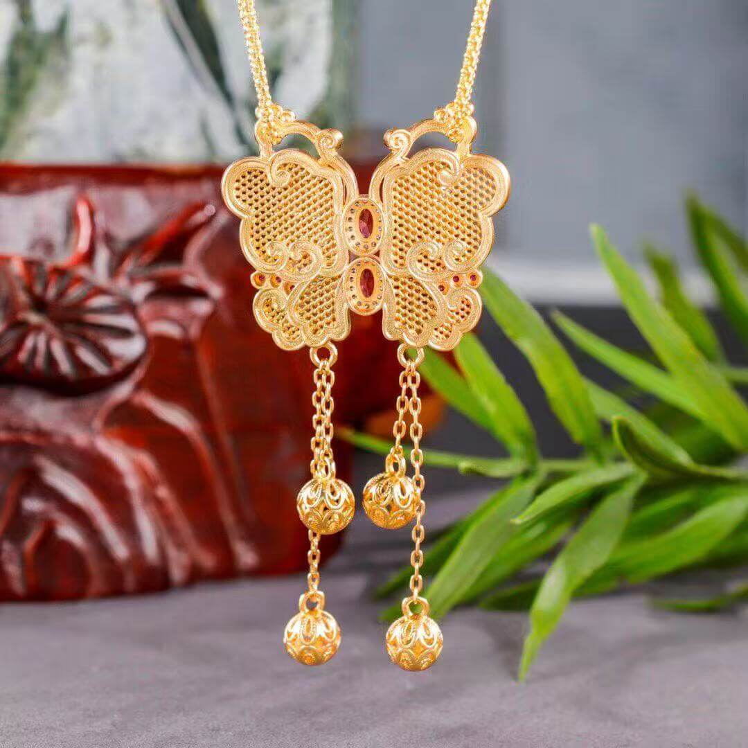 Gold butterfly necklace with dangling beads on a gray surface with green leaves in the background