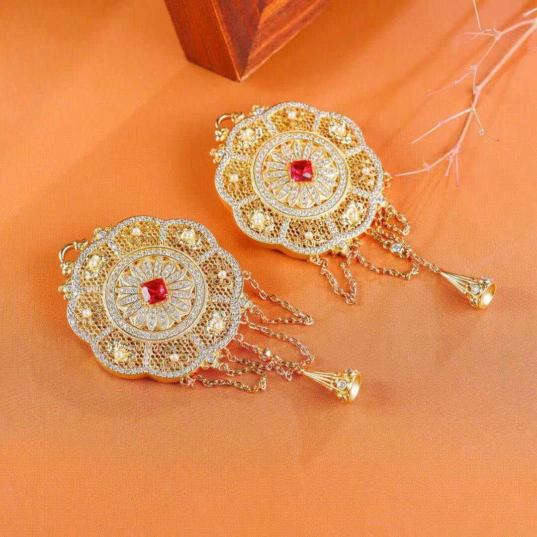 Ornate gold earrings with red gemstones on an orange background